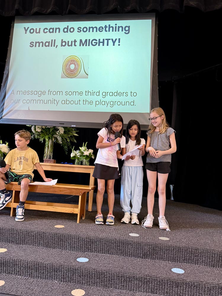 3 3rd Grade Girls reading a letter at a school meeting