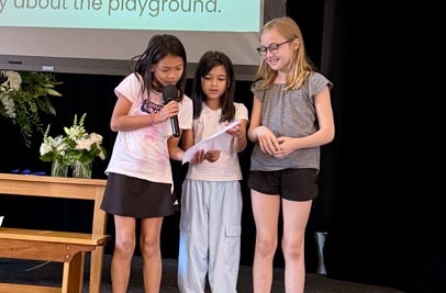 3 3rd Grade Girls reading a letter at a school meeting